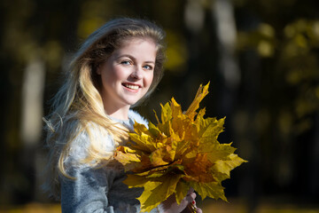 Beautiful young woman in an autumn park with a bouquet of maple leaves.