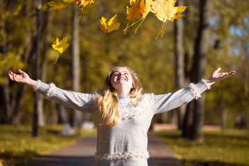 Beautiful young woman in an autumn park scatters maple leaves.