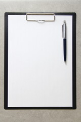 Template of white paper with a ballpoint pen on light grey concrete background in a black tablet with a clip. Concept of new idea, business plan and strategy, empty space for text