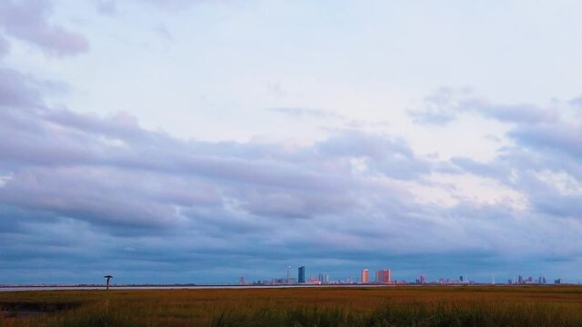 HD MOTIONLAPSE Pan and tilt from upper left to lower right Atlantic City skyline in distance over waterway with mostly cloudy sky day to night with clouds turning pink, purple and blue