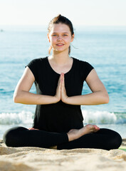 Fototapeta na wymiar Fitness woman in black T-shirt is sitting and doing yoga on the beach.