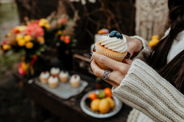 a woman's hand holds a sweet delicious muffin, a cupcake with white cream and blueberries in the hands of a girl, take a meal, a delicious sweet treat dessert, enjoyment, a pleasant moment