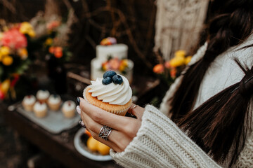 a woman's hand holds a sweet delicious muffin, a cupcake with white cream and blueberries in the hands of a girl, take a meal, a delicious sweet treat dessert, enjoyment, a pleasant moment