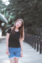 Teenage woman makes a funny face and stands smiling on the street. People wear casual clothes in a black T-shirt and shorts. Women walking in nature. Tone film.