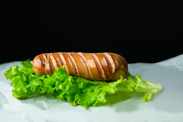 Toasted sausage with a lettuce on white paper on black background