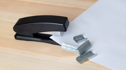 Stapler and staples with sheets of paper a wooden table.