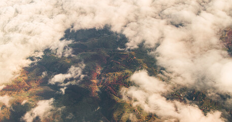 Fototapeta premium Aerial airplane view between the clouds of a lot of forests in autumn colors