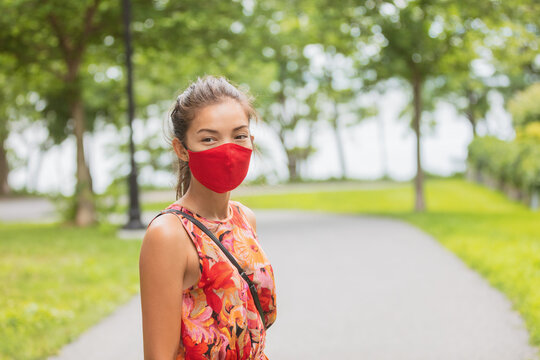 Asian woman wearing facial covering walking on street while waiting outside bus stop for public transport. Summer fashion portrait in red mask.