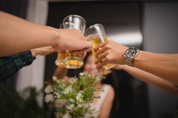 Close-up of hands of a group of Asian people having a party at home. They clink a glass of beer.