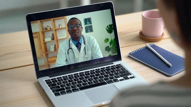 Telemedicine conference on laptop. Patient talk to African doctor from home. Spbas View over shoulder, coronavirus sick person consulting with physician. Concept of telehealth, video call, computer