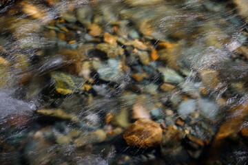 Rocky bottom of mountain river through the clear water, selective focus, blurring the image. Cristal water in the stream shimmers in sunlight. Stone background.
