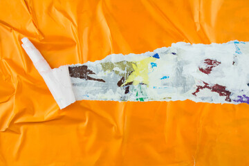 Torn, crumpled and peeling orange magazine paper poster on surface with old ripped pieces of paper...