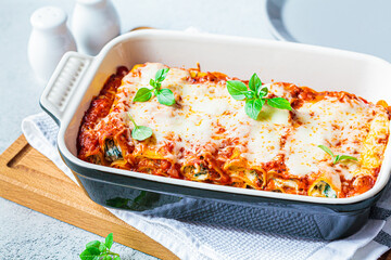 Traditional ricotta and spinach cannelloni in ceramic dish on wooden board. Italian food concept.