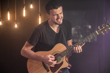 Happy guitarist in a black t-shirt plays an acoustic guitar at a concert against a blurred black background. Close up.