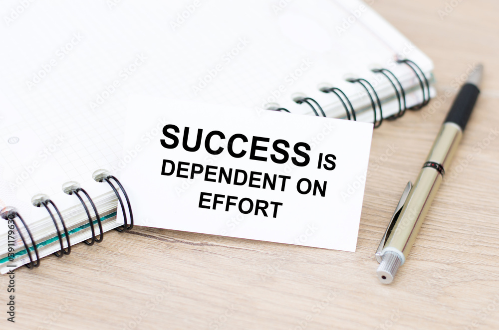 Aufkleber business card with success is dependent on effort text on the table, next to a notebook and a pen.