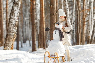 happy child girl plaing with a snowman on a snowy winter walk