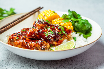 Asian food concept. Sticky sesame  chicken with rice and vegetables in white plate, gray background.