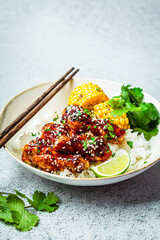 Asian food concept. Sticky sesame  chicken with rice and vegetables in white plate, gray background.