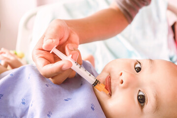  Asian infant receives medicine with a syringe into his mouth. Focus on face