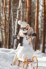 happy child girl plaing with a snowman on a snowy winter walk