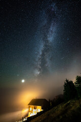 Cosy house and milky way beyond the clouds at night starry sky 