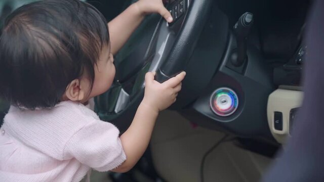 Asian female Child wondering playing inside the car, kids development learning skills, vehicle playing with steering wheel, baby sitting on car driver seat, happy infant girl pretend to be a driver