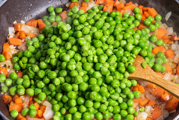 Cooking pasta with peas and carrots - cooking sauce of peas, carrots and onions in a frying pan.
