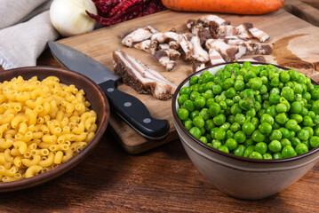 Ingredients for making pasta with peas and pancetta on a rustic wooden table - pancetta, bacon, peas, onions, carrots, chifferini