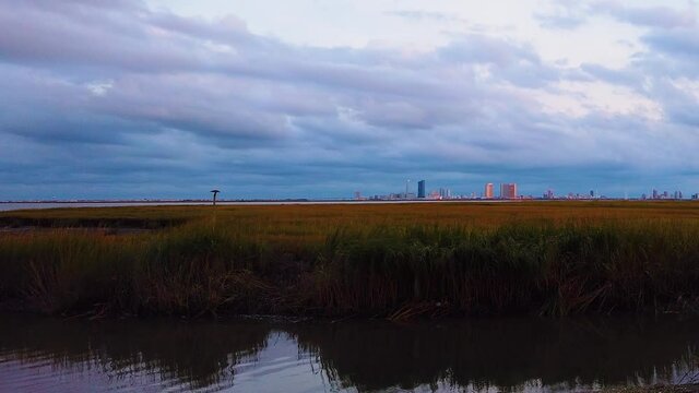 HD MOTIONLAPSE Straight pan from left to right Atlantic City skyline in distance over waterway with mostly cloudy sky day to night with clouds turning pink, purple and blue