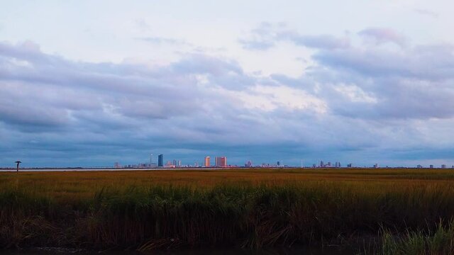 HD MOTIONLAPSE Zoom out and hold Atlantic City skyline in distance over waterway with mostly cloudy sky day to night with clouds turning pink, purple and blue