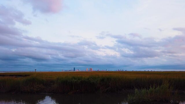 HD MOTIONLAPSE Zoom in Atlantic City skyline in distance over waterway with mostly cloudy sky day to night with clouds turning pink, purple and blue