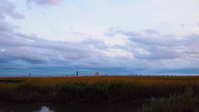HD MOTIONLAPSE Zoom in and hold Atlantic City skyline in distance over waterway with mostly cloudy sky day to night with clouds turning pink, purple and blue