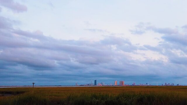 HD MOTIONLAPSE Pan and tilt from upper left to center Atlantic City skyline in distance over waterway with mostly cloudy sky day to night with clouds turning pink, purple and blue