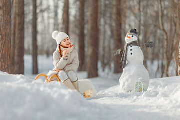 happy child girl plaing with a snowman on a snowy winter walk