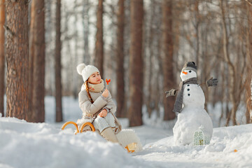 happy child girl plaing with a snowman on a snowy winter walk