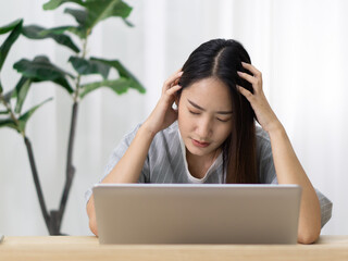 Young asian woman held her head with both hands due to headaches from using computer for a long time.