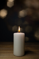 Fototapeta na wymiar A white burning candle on a wooden table, lensflares background and copy space