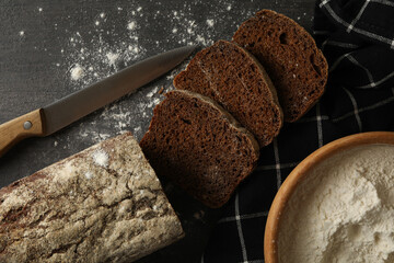 Rye bread, knife, napkin and flour on black background