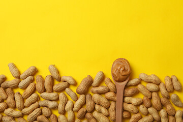 Peanut and spoon with peanut butter on yellow background