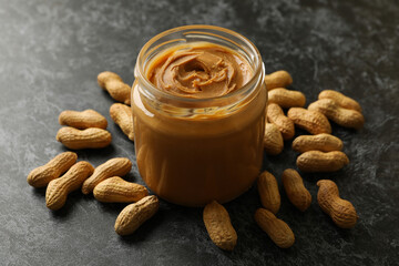 Peanut and jar with peanut butter on black smoky background