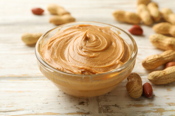 Peanut and bowl with peanut butter on wooden background