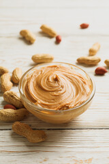 Peanut and bowl with peanut butter on wooden background