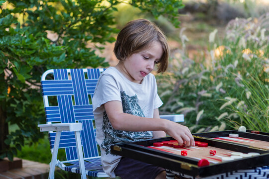 A young boy playing backgammon outdoors in a garden. 
