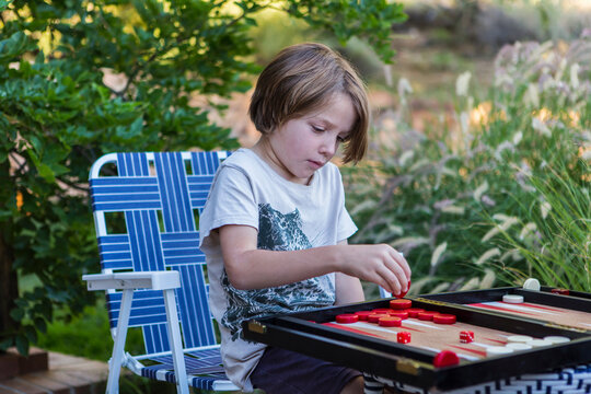 A young boy playing backgammon outdoors in a garden. 