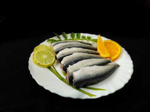 Cleaned and ready to cook fresh indian sardine decorated with curry leaves,lemon slice and tomato slice .Isolated on black background.