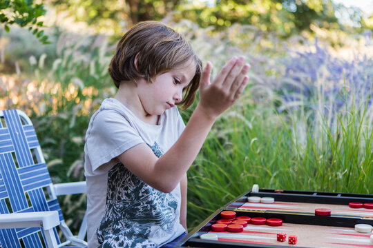 A young boy playing backgammon outdoors in a garden. 