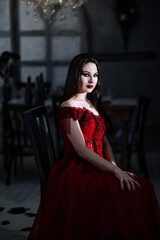 Fototapeta na wymiar Bloodthirsty female vampire in red dress. Medieval interior