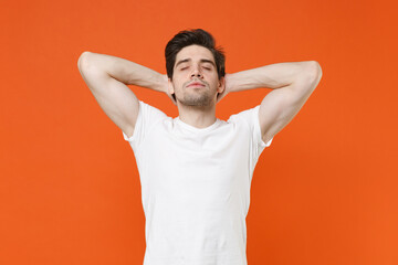 Fototapeta na wymiar Relaxed tired young man 20s wearing basic casual white blank empty t-shirt standing sleep with hands behind head keeping eyes closed isolated on bright orange colour wall background, studio portrait.