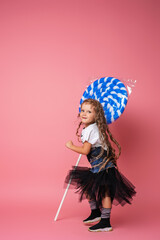 Stylish little girl with curly hair and large pink Lollipop on pink background.