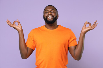 Smiling young african american man 20s in casual orange blank empty t-shirt hold hands in yoga...